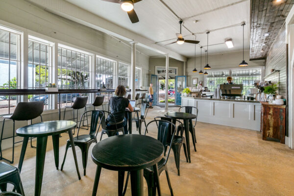 A woman works remotely on her laptop while the barista makes her coffee.